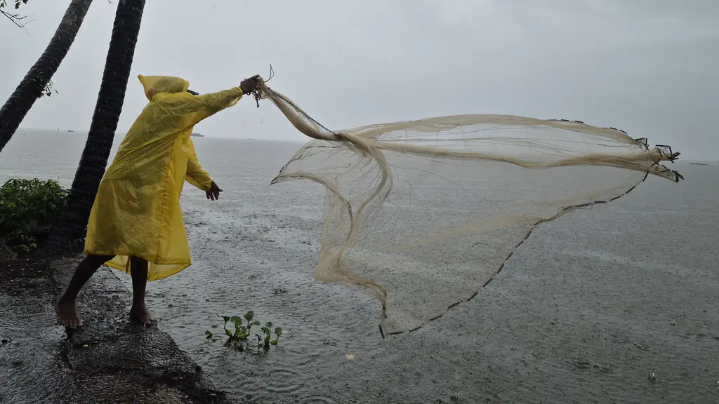 A fisherman in a yellow raincoat casts a net over a lake in the rain