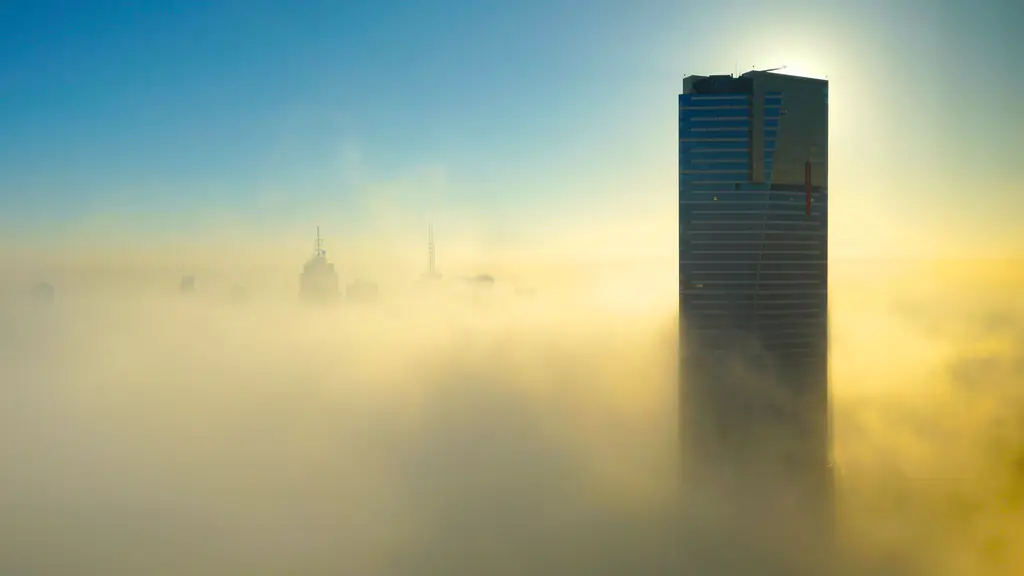 A glass skyscraper rises above a sea of golden morning fog, the low sun flaring behind its top