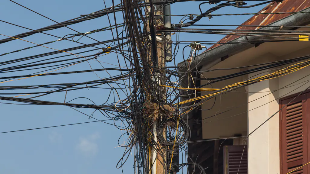 Black and yellow cables knotted around a wooden utility pole against a blue sky, beside a shuttered house